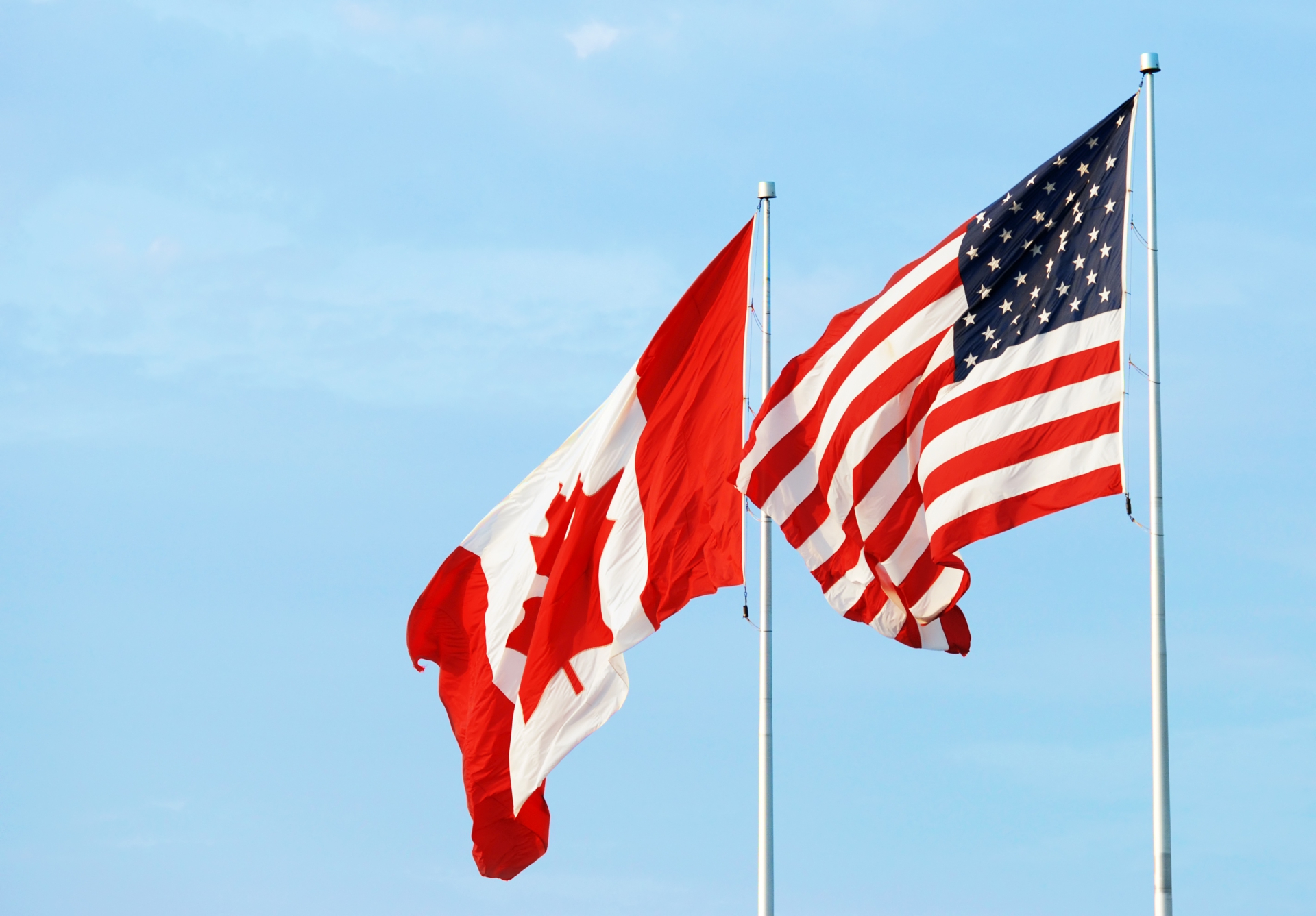 A Candian Flag and American Flag blowing in the wind.